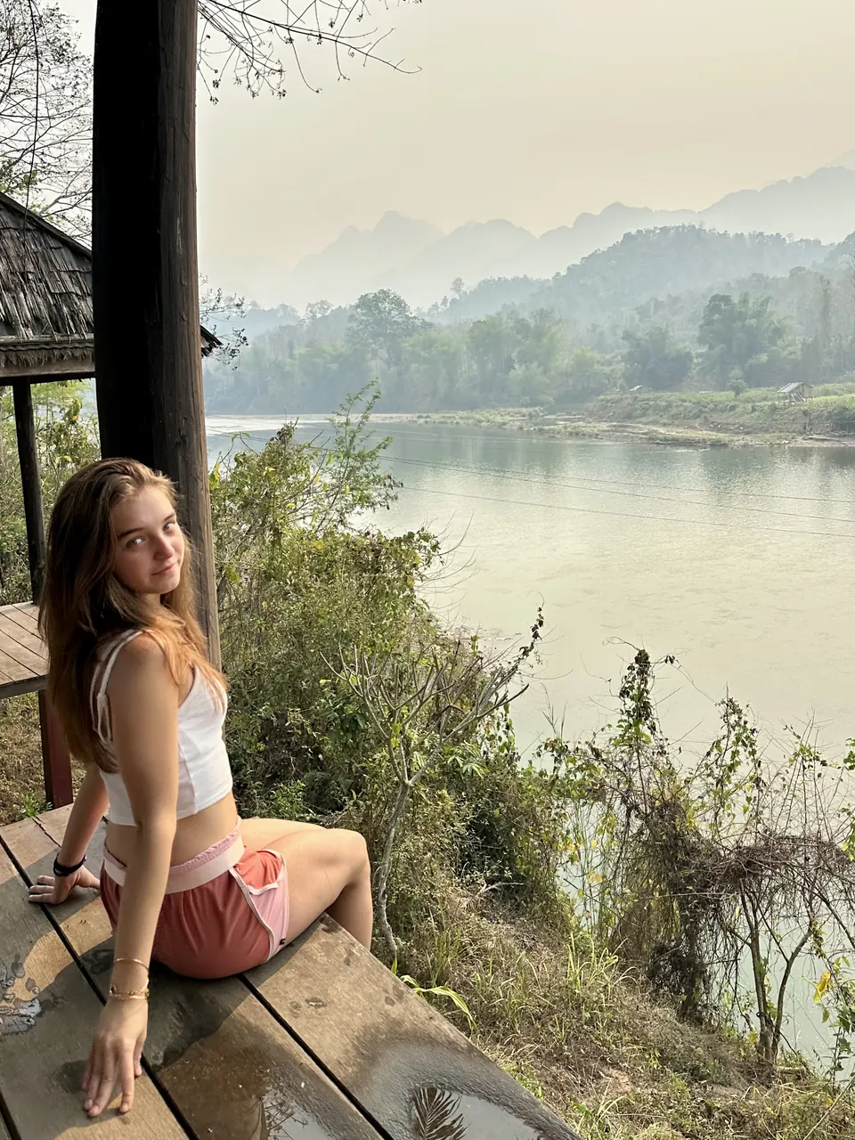 Manon Maindivide casual photo sitting on a wooden deck above a misty river and green hills