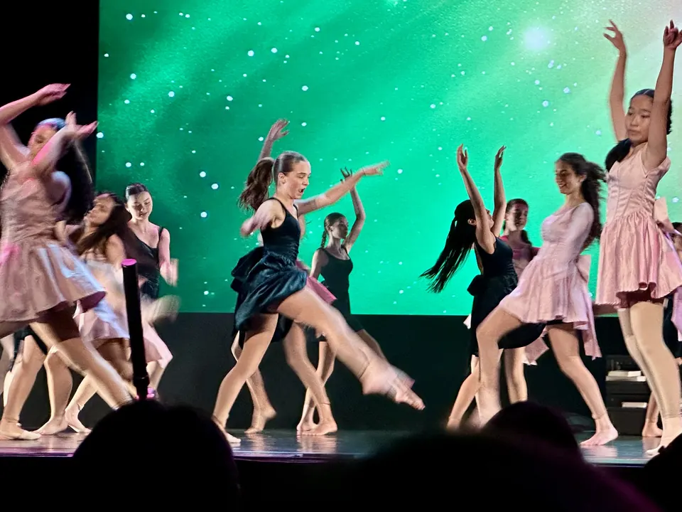 Manon Maindivide dance performance with a group in pink and black dresses before a green starry backdrop