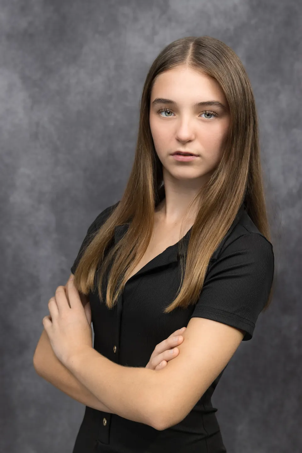 Manon Maindivide headshot in a black shirt with arms crossed against a grey studio backdrop
