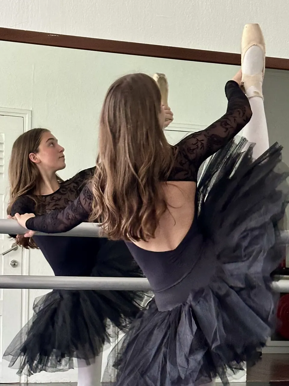 Manon Maindivide dance rehearsal at the barre in a black tutu, leg extended high by the mirror