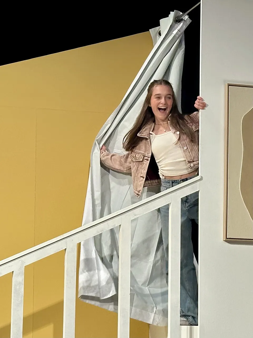 Manon Maindivide on stage in a pink jacket, bursting through a door on a white staircase set