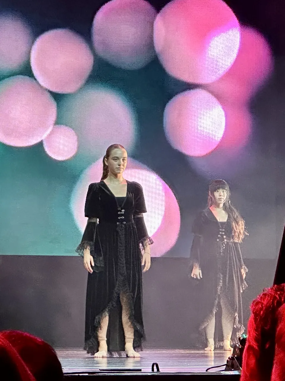 Manon Maindivide on stage in a long black costume under pink bokeh lights