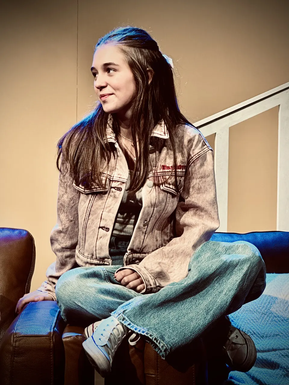 Manon Maindivide on stage in a denim jacket and jeans, sitting cross-legged on a sofa