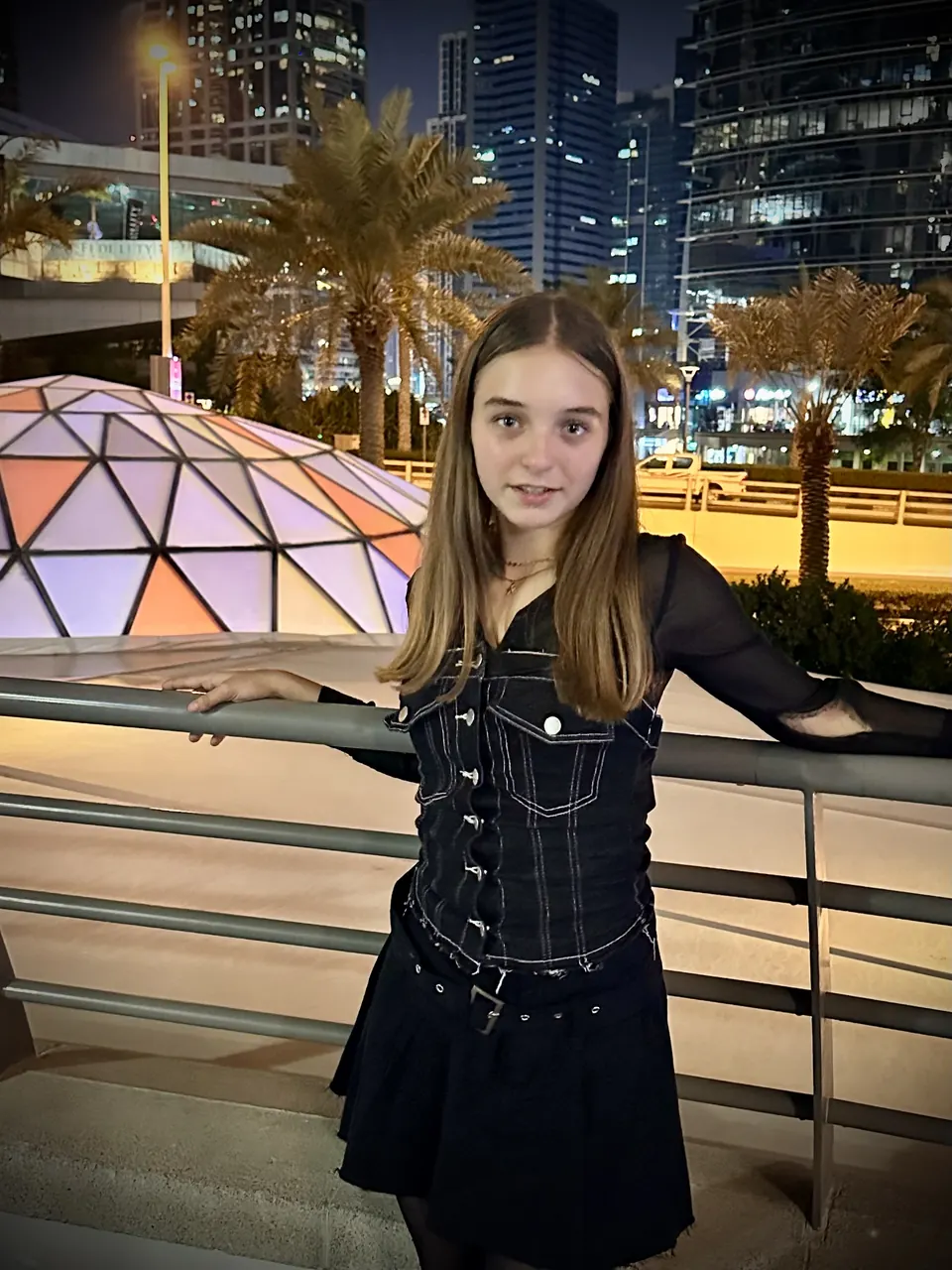 Manon Maindivide casual photo in a black denim dress at night, city lights and palm trees behind