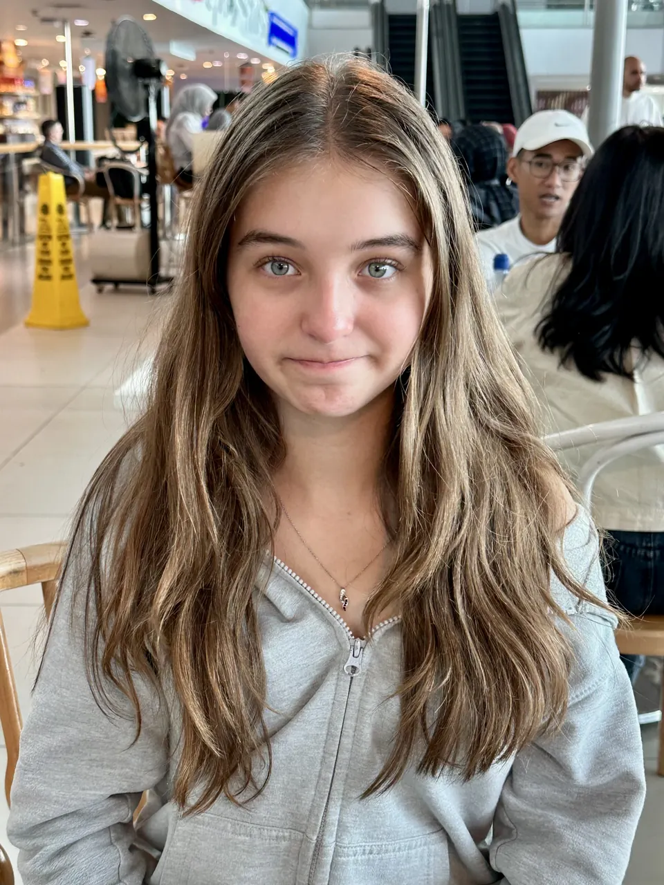 Manon Maindivide casual portrait in a grey zip hoodie, smiling in a busy airport terminal