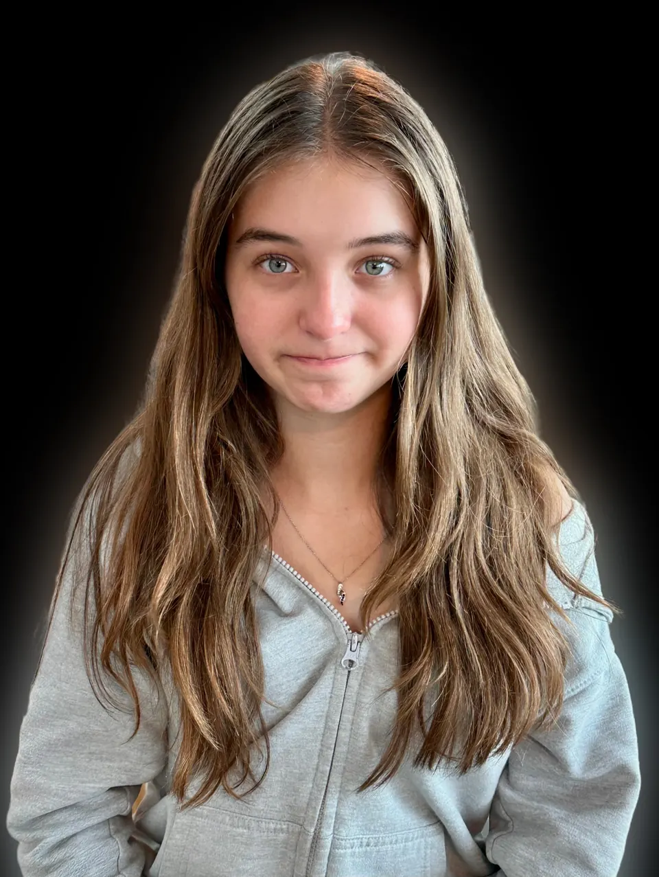 Manon Maindivide headshot in a grey zip hoodie with long hair, soft smile on a black background