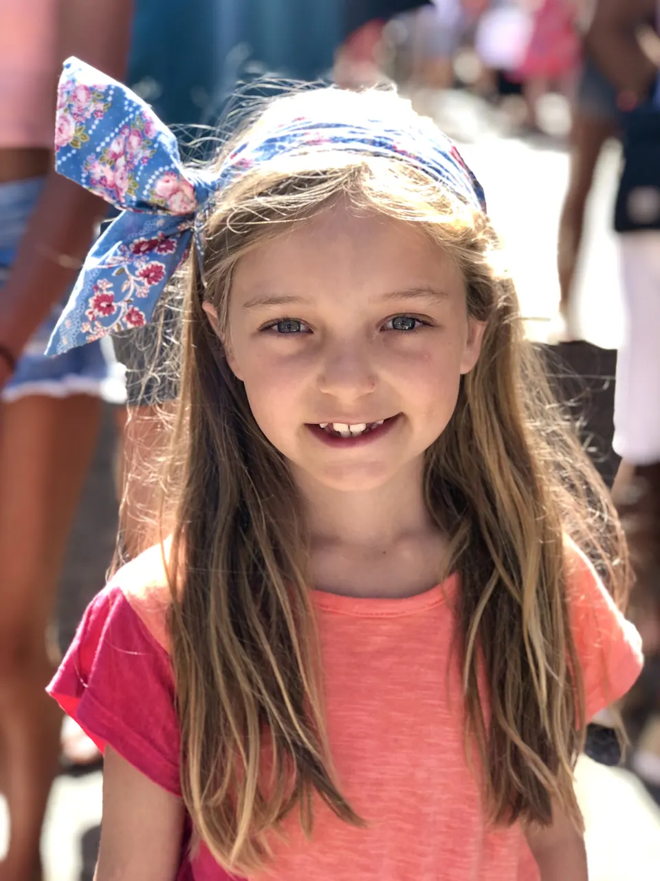 Manon Maindivide casual portrait in a coral tee and floral headscarf, smiling outdoors in the sun