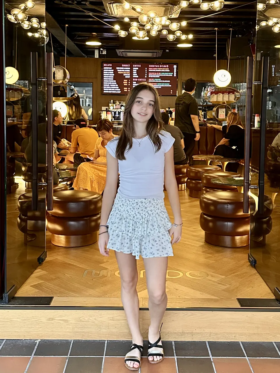 Manon Maindivide casual photo at the entrance of a restaurant, wearing a white top and floral skirt