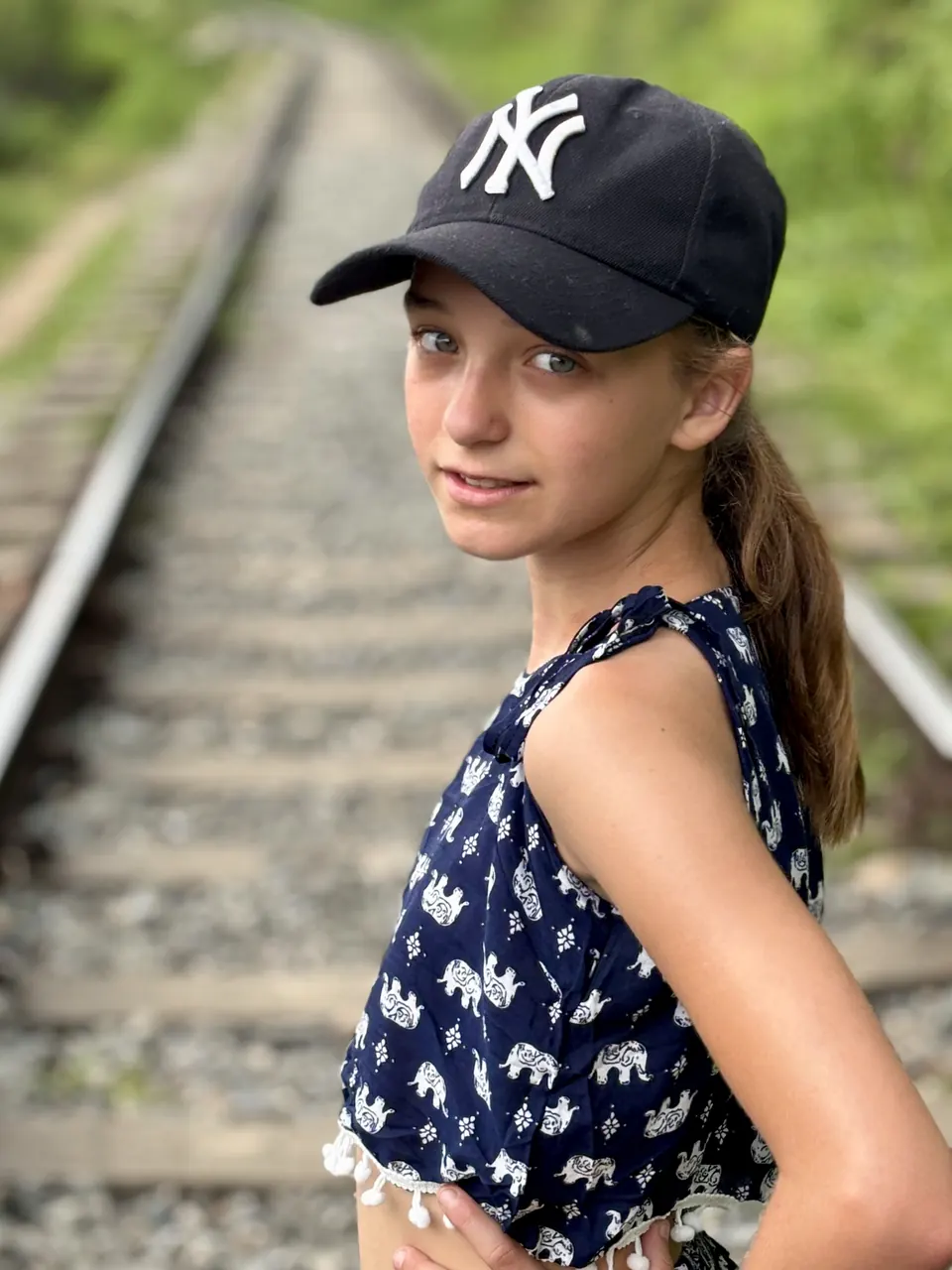 Manon Maindivide photo shoot beside railway tracks, wearing a navy cap and a patterned sleeveless top