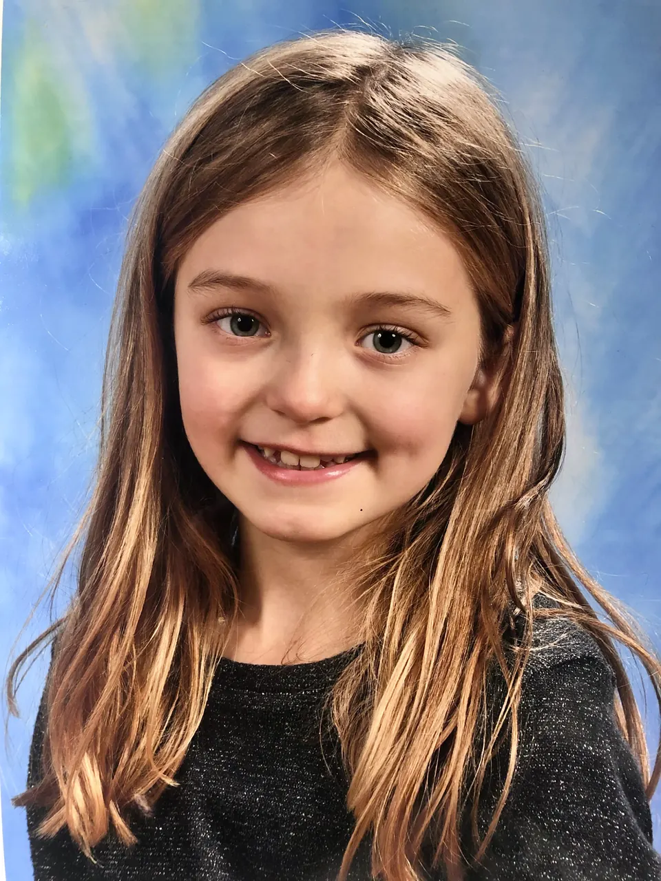 Manon Maindivide headshot as a young child, smiling in a dark top against a blue painted backdrop