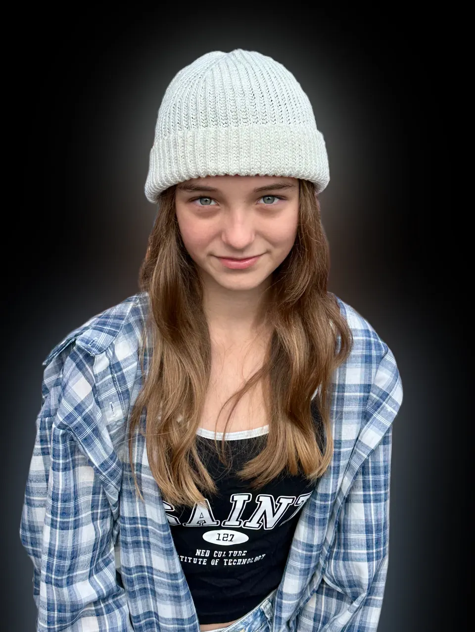 Manon Maindivide headshot in a grey knit beanie and plaid shirt against a dark background