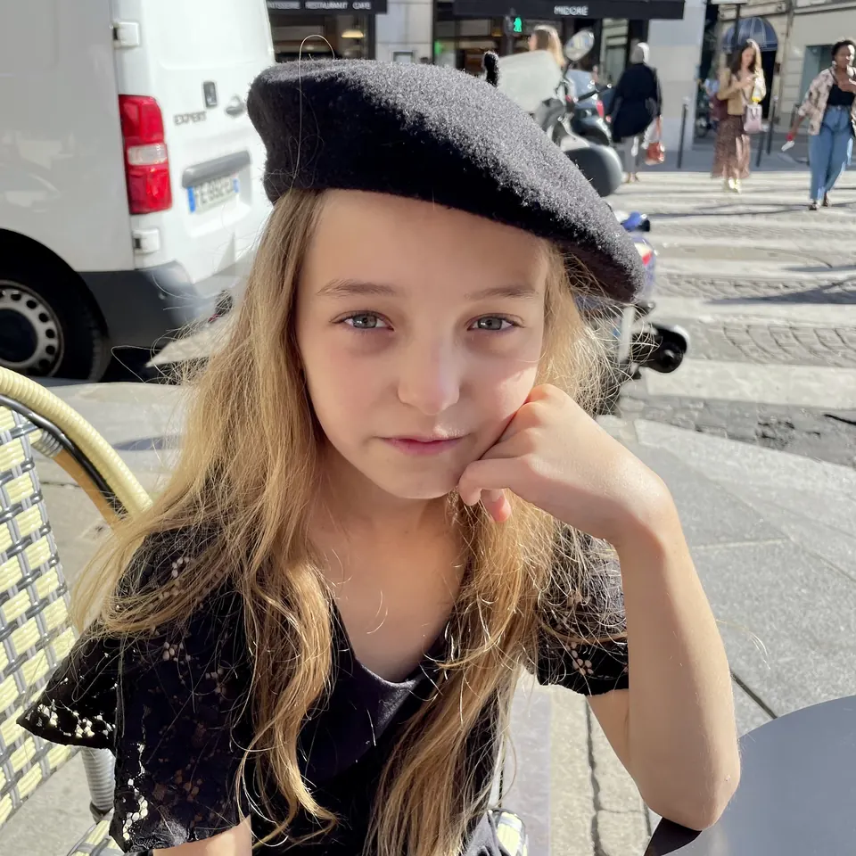 Manon Maindivide casual portrait in a black beret, chin on hand at a sunny street cafe
