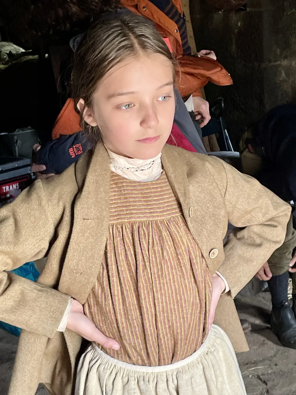 Manon Maindivide on set in a period costume with a tweed jacket and lace collar, hands on hips