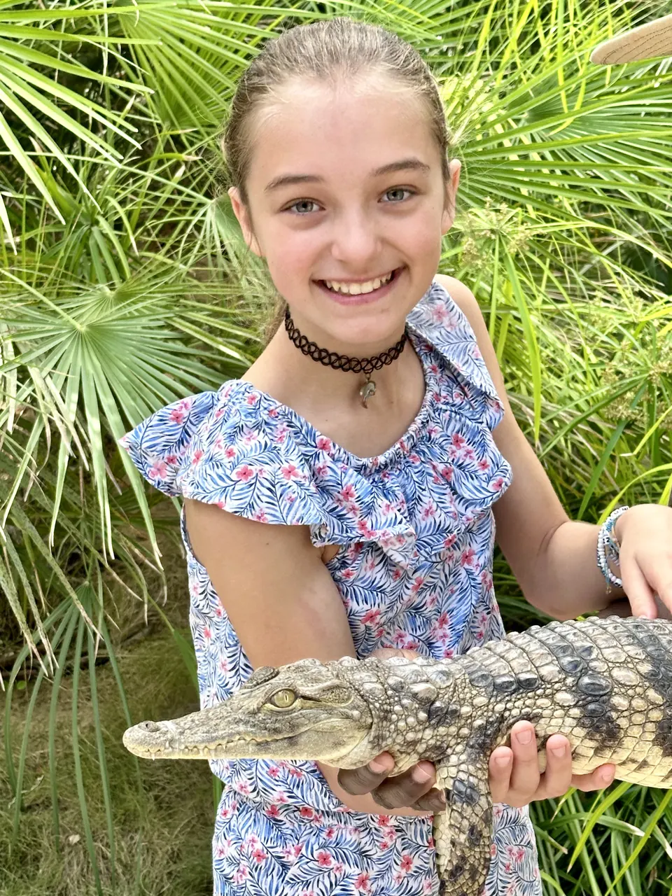 Manon Maindivide casual photo holding a small crocodile, wearing a floral dress among palm leaves