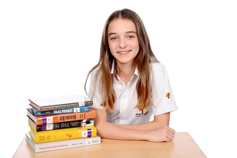 Manon Maindivide portrait in a white shirt, leaning on a table beside a stack of books