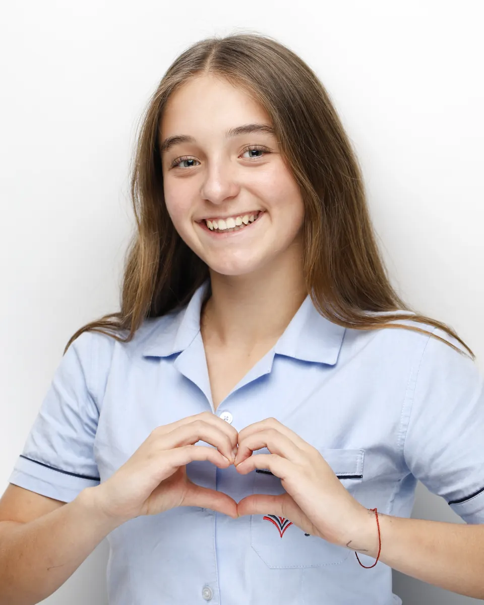 Manon Maindivide headshot in a light blue shirt, smiling and making a heart with her hands