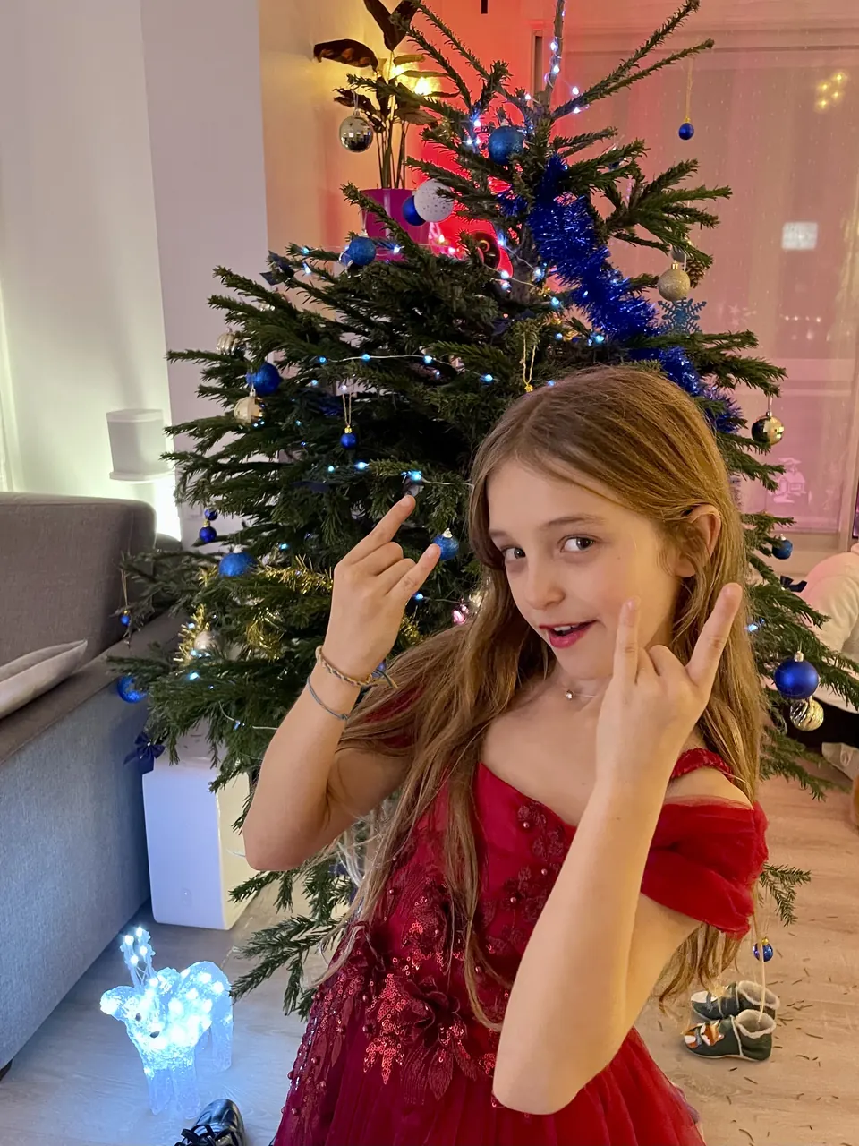 Manon Maindivide casual photo in a red dress by a Christmas tree, making a playful hand sign