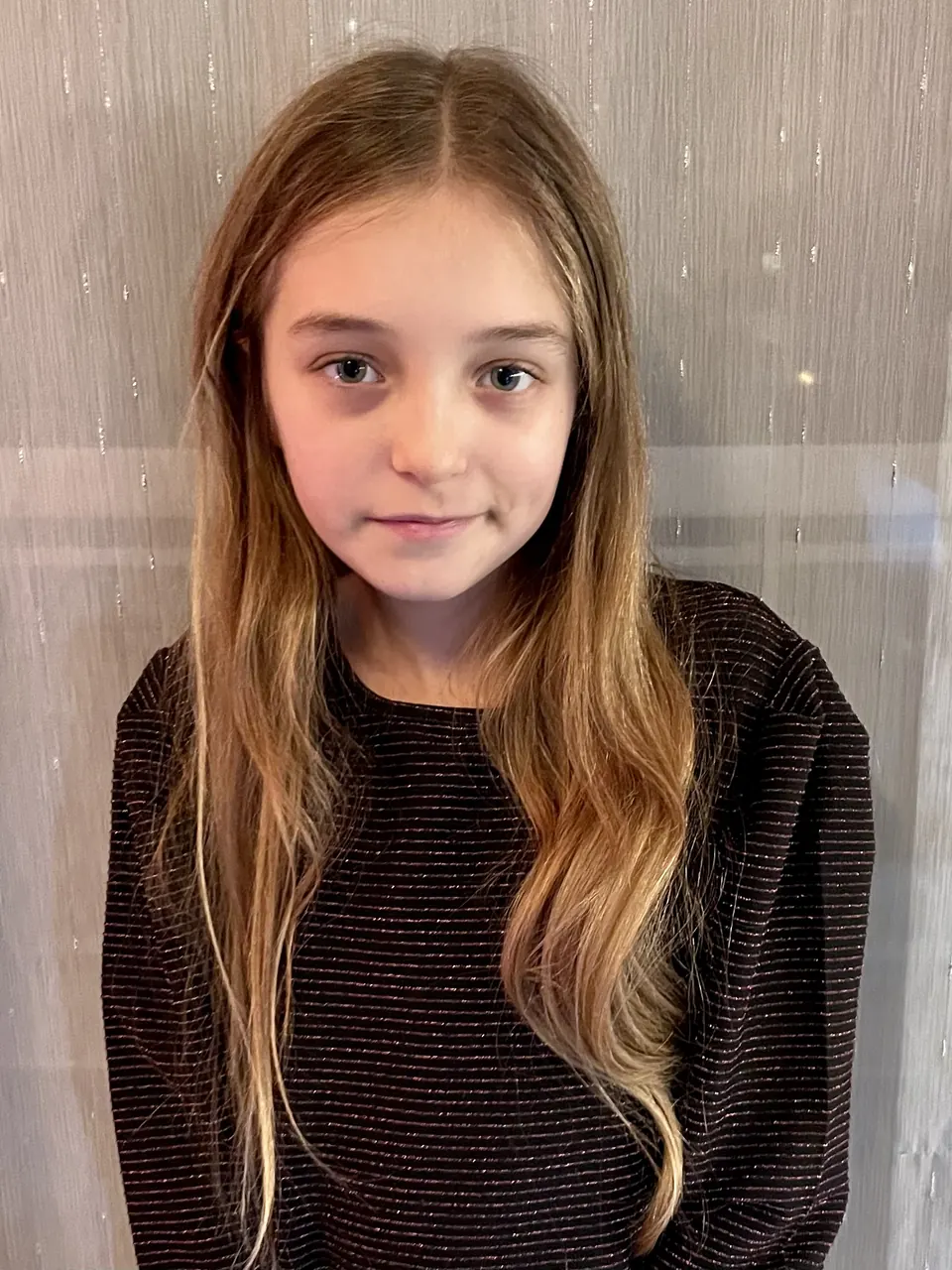 Manon Maindivide headshot in a dark sparkly sweater with long hair against a light grey wall