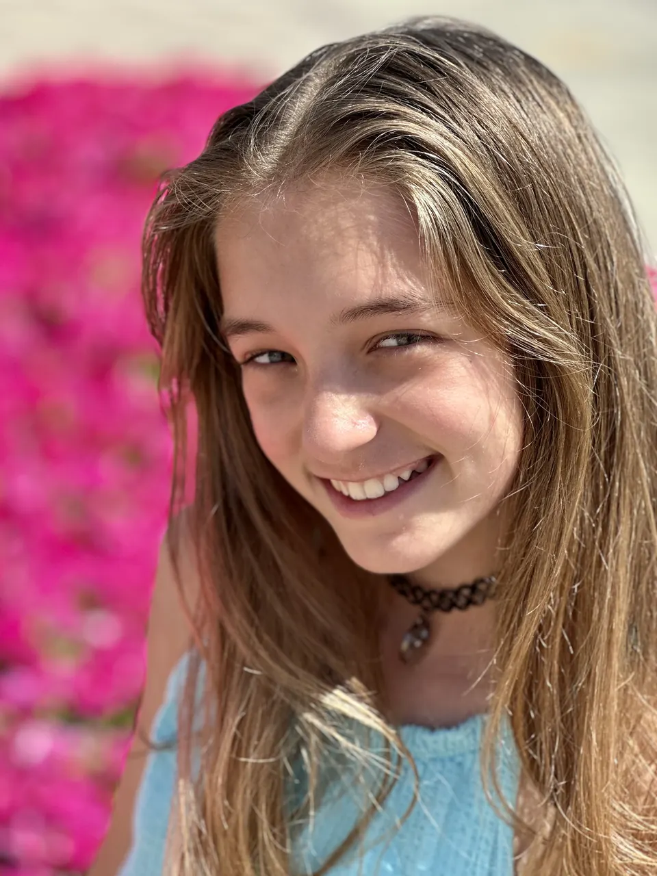 Manon Maindivide casual portrait with a black choker, smiling in front of pink flowers