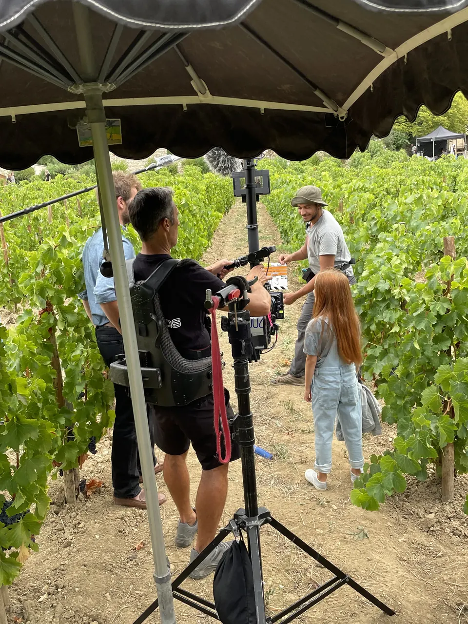 Manon Maindivide on set in a vineyard, crew with a camera rig and a shade umbrella nearby