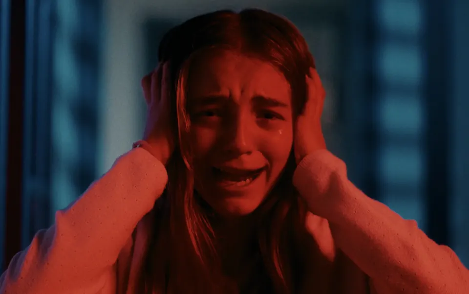 Manon Maindivide on set in an intense film scene, crying with hands on her head in red light