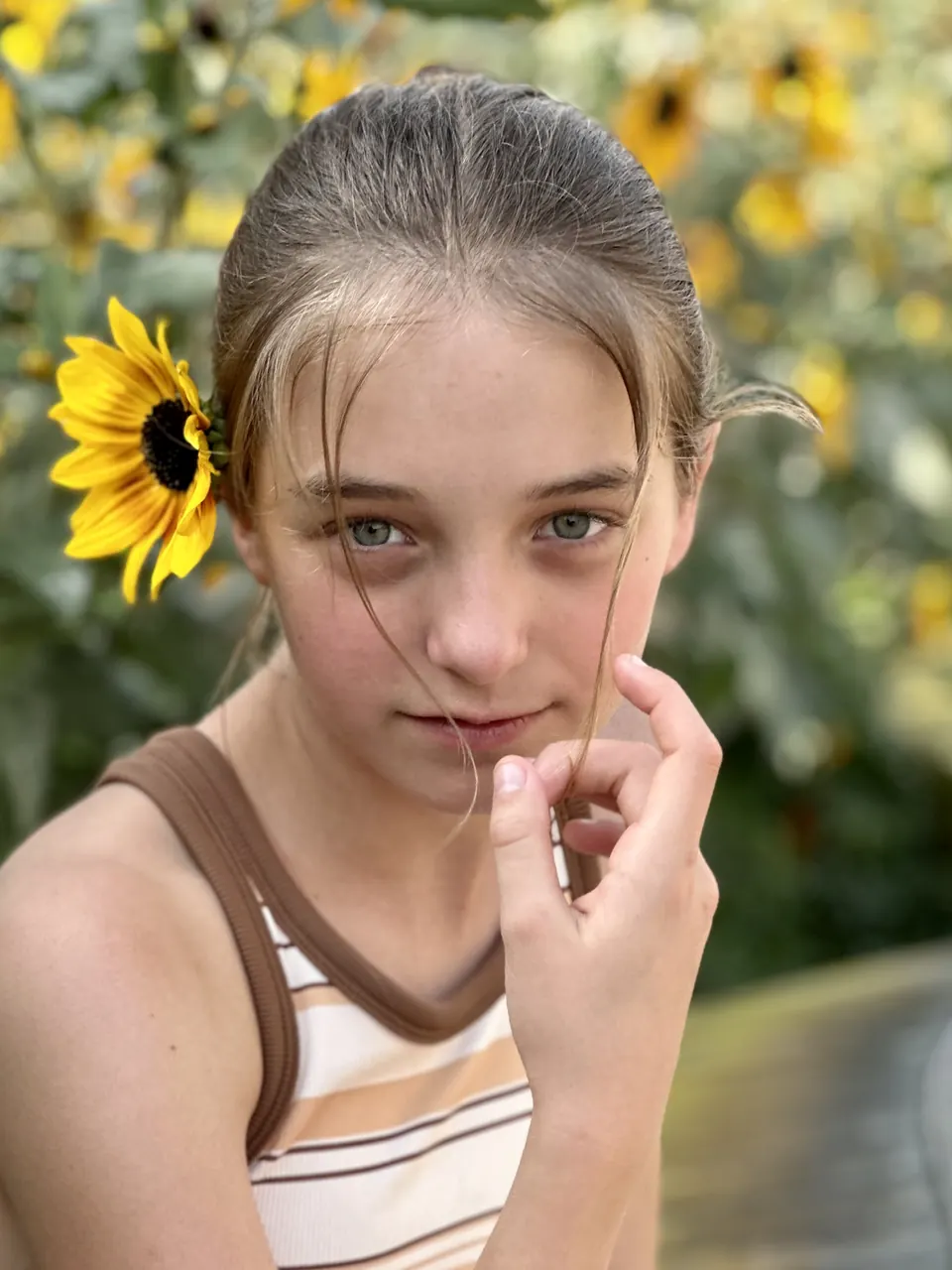 Manon Maindivide portrait with a sunflower in her hair, hand near her face, in a striped tank top