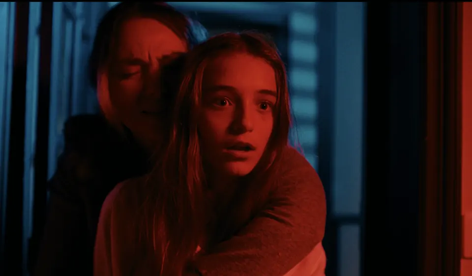 Manon Maindivide on set in a dramatic film scene with red lighting, held by an adult actor