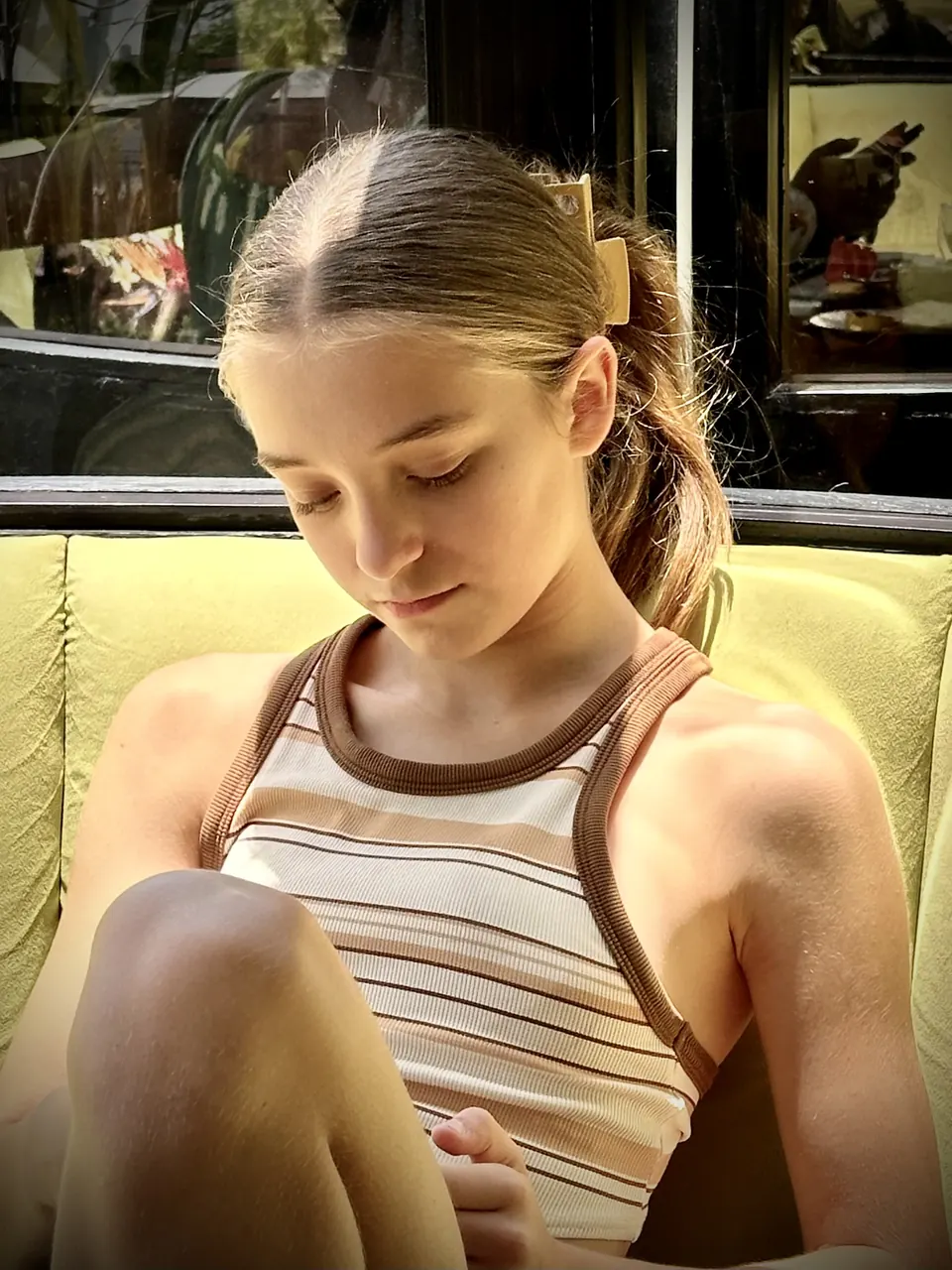 Manon Maindivide portrait in a striped tank top on a yellow chair, looking down in soft warm light