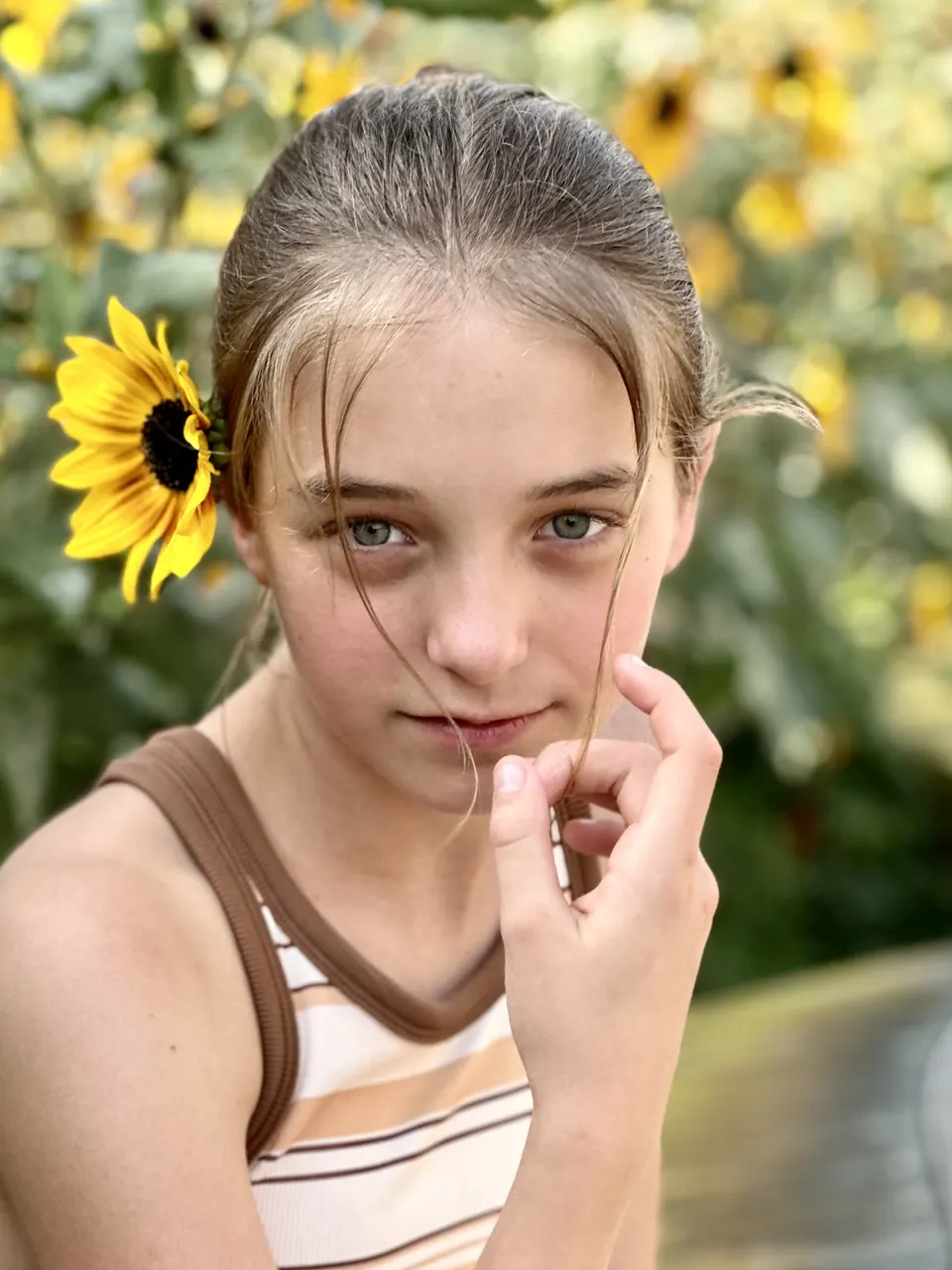 Manon Maindivide close-up portrait with a sunflower tucked behind her ear, gazing into the camera