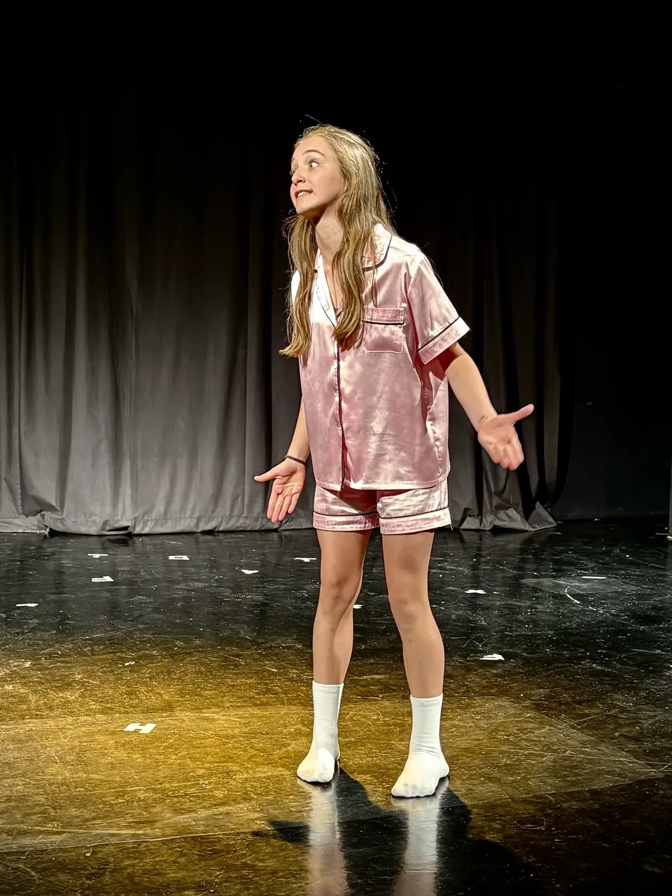 Manon Maindivide on stage in pink pyjamas, looking up with a surprised expression under spotlights