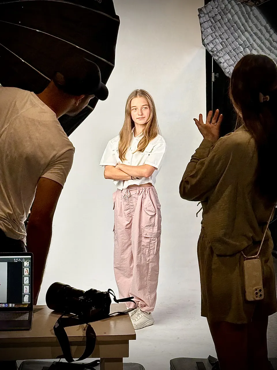 Manon Maindivide behind the scenes of a studio photo shoot, posing in pink trousers as crew work