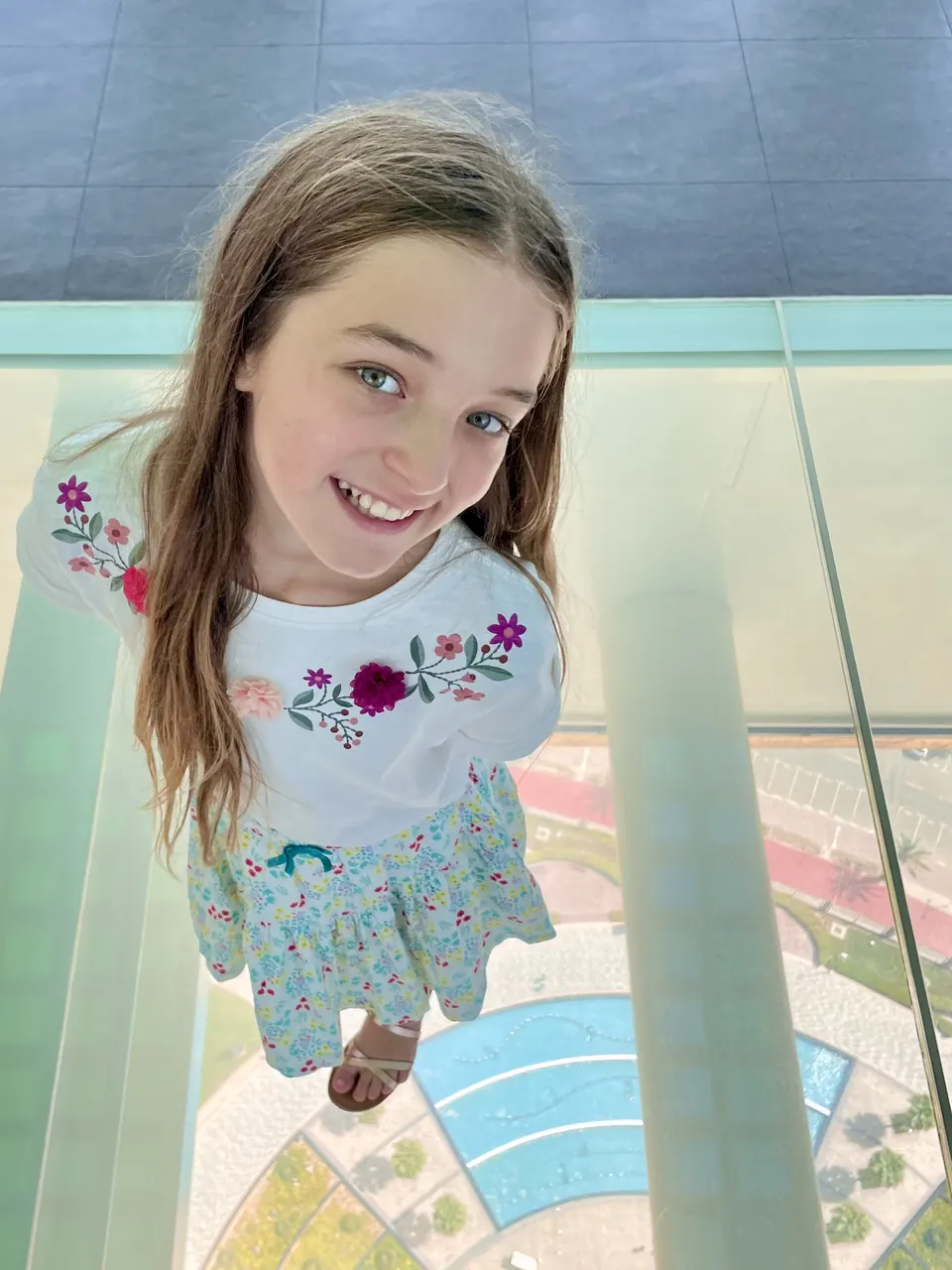 Manon Maindivide casual photo taken from above, smiling in a floral embroidered top on a glass floor