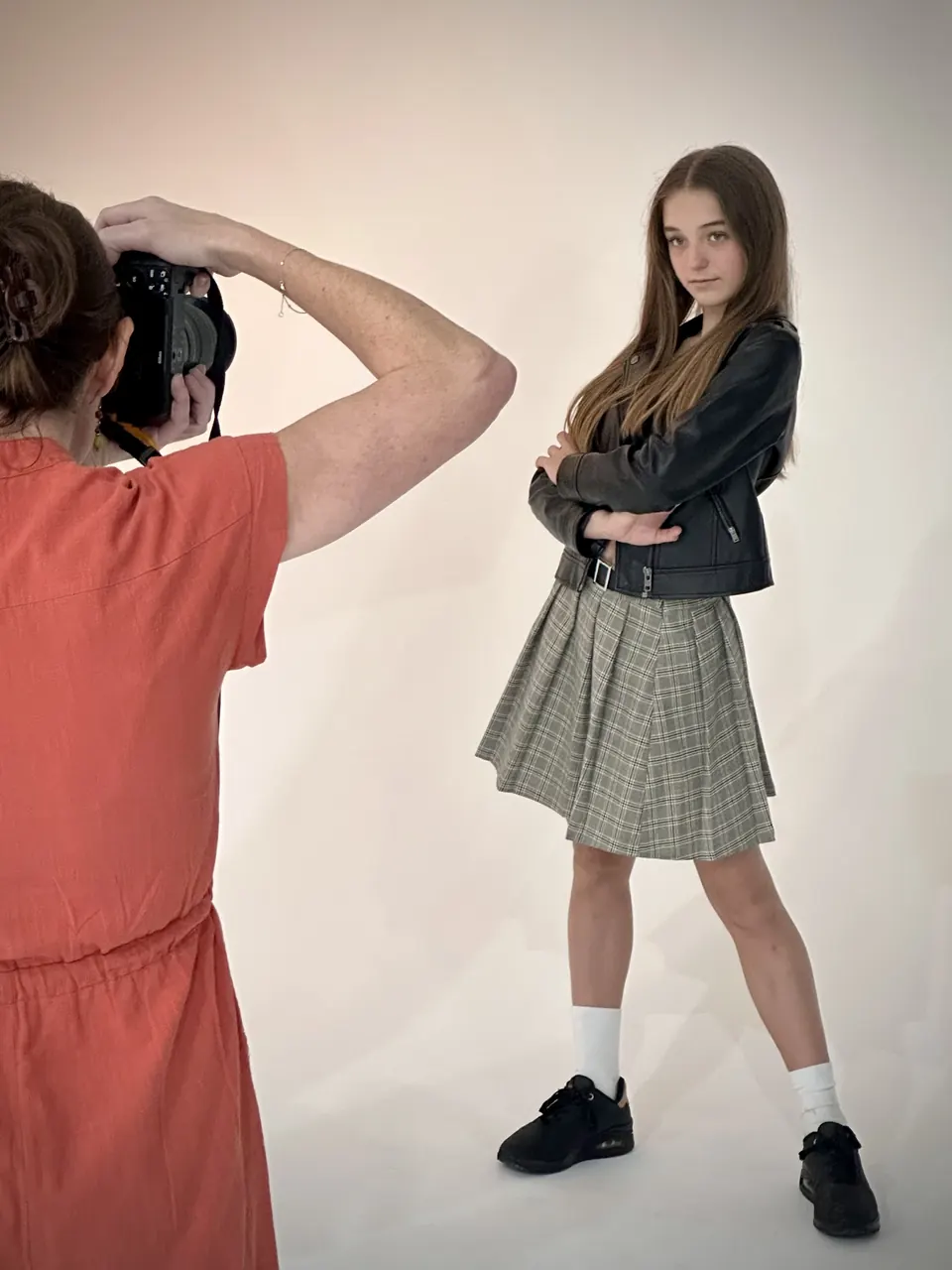 Manon Maindivide behind the scenes of a photo shoot in a leather jacket and plaid skirt, photographer in view