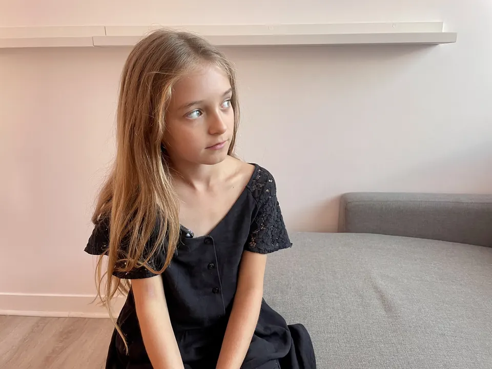 Manon Maindivide portrait sitting on a grey sofa in a black dress, looking away with a calm expression