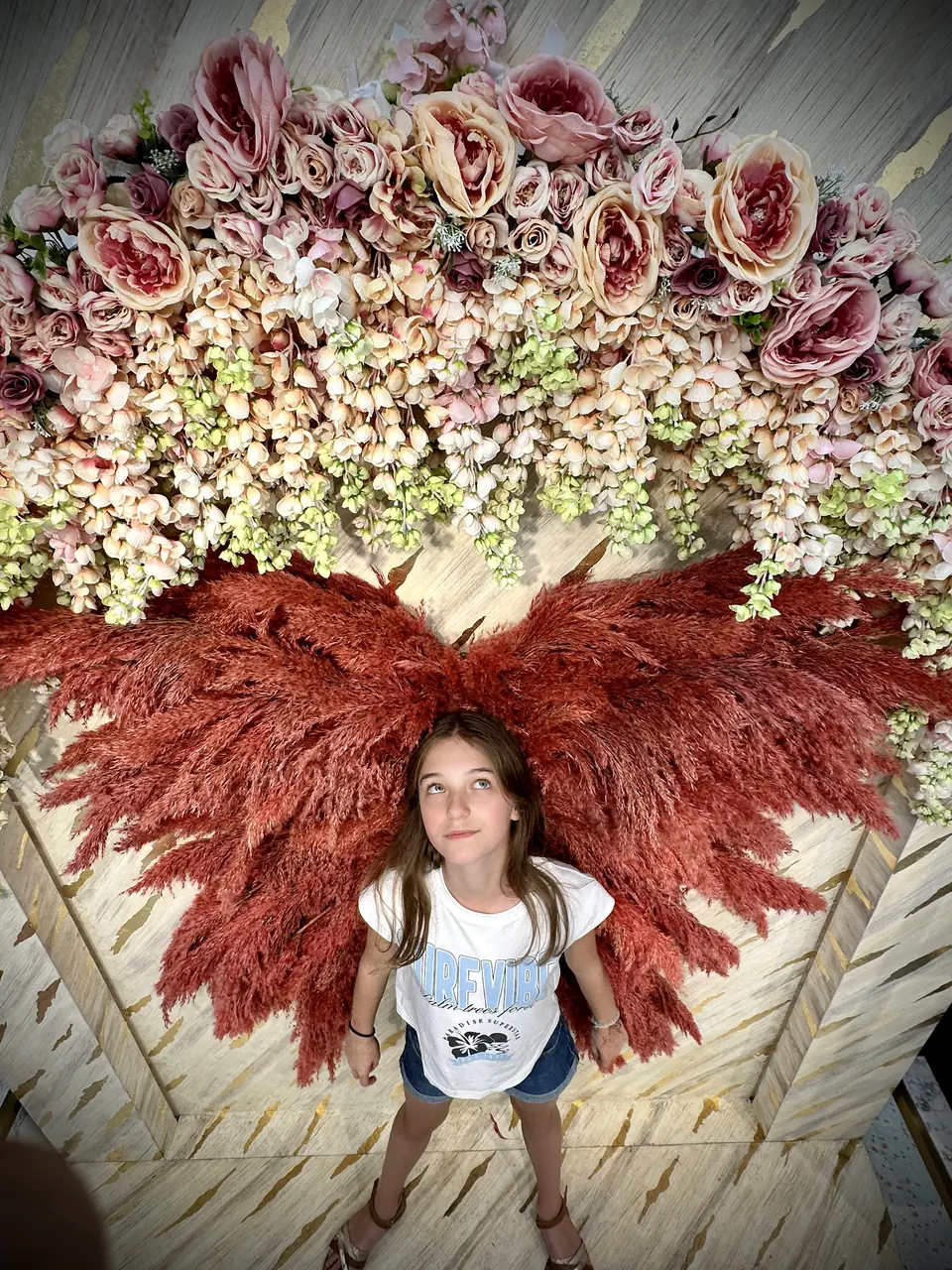 Manon Maindivide photo shoot, standing beneath a large installation of dried flowers and red plumes