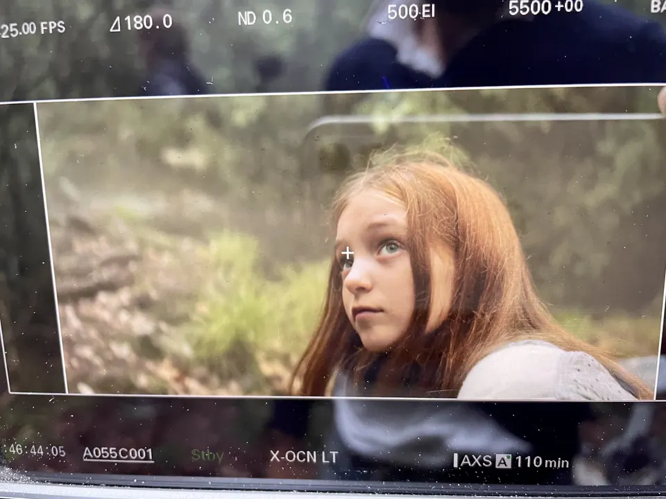 Manon Maindivide on set, framed on a camera monitor gazing up in a green forest scene