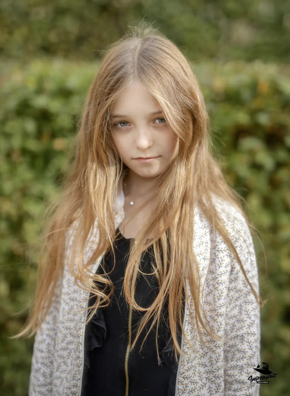 Manon Maindivide portrait with long blonde hair and a speckled cardigan in front of green hedges