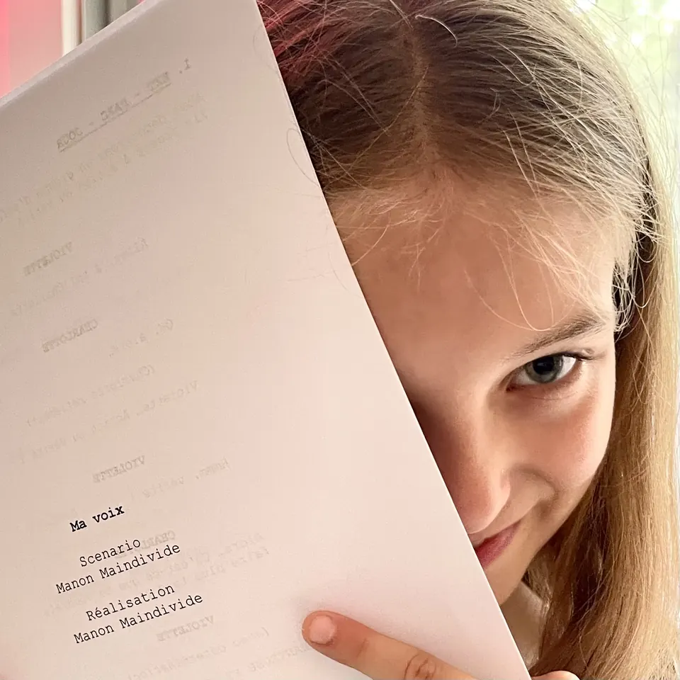 Manon Maindivide behind the scenes, half her face hidden behind a printed screenplay page