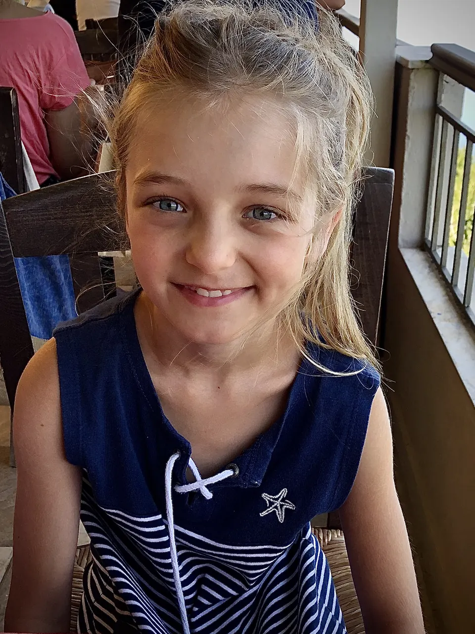 Manon Maindivide casual portrait smiling in a navy sleeveless top at a wooden cafe table