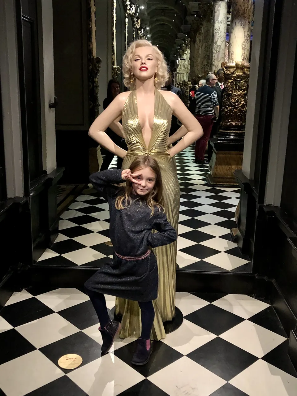 Manon Maindivide casual photo on a checkered floor posing in front of a gold-gowned wax figure