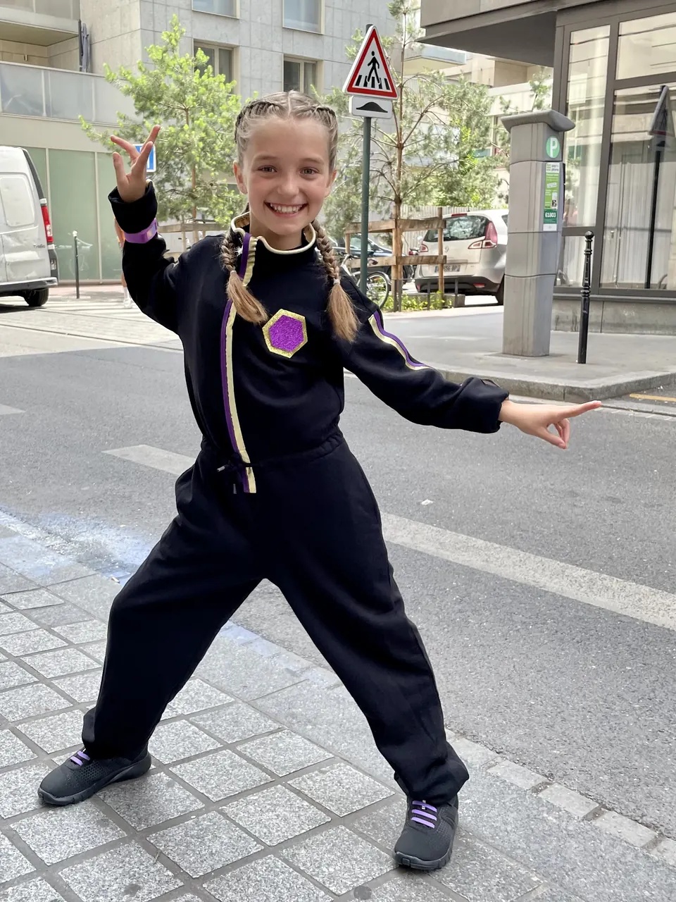 Manon Maindivide behind the scenes on a city street in a black costume with braids, striking a pose