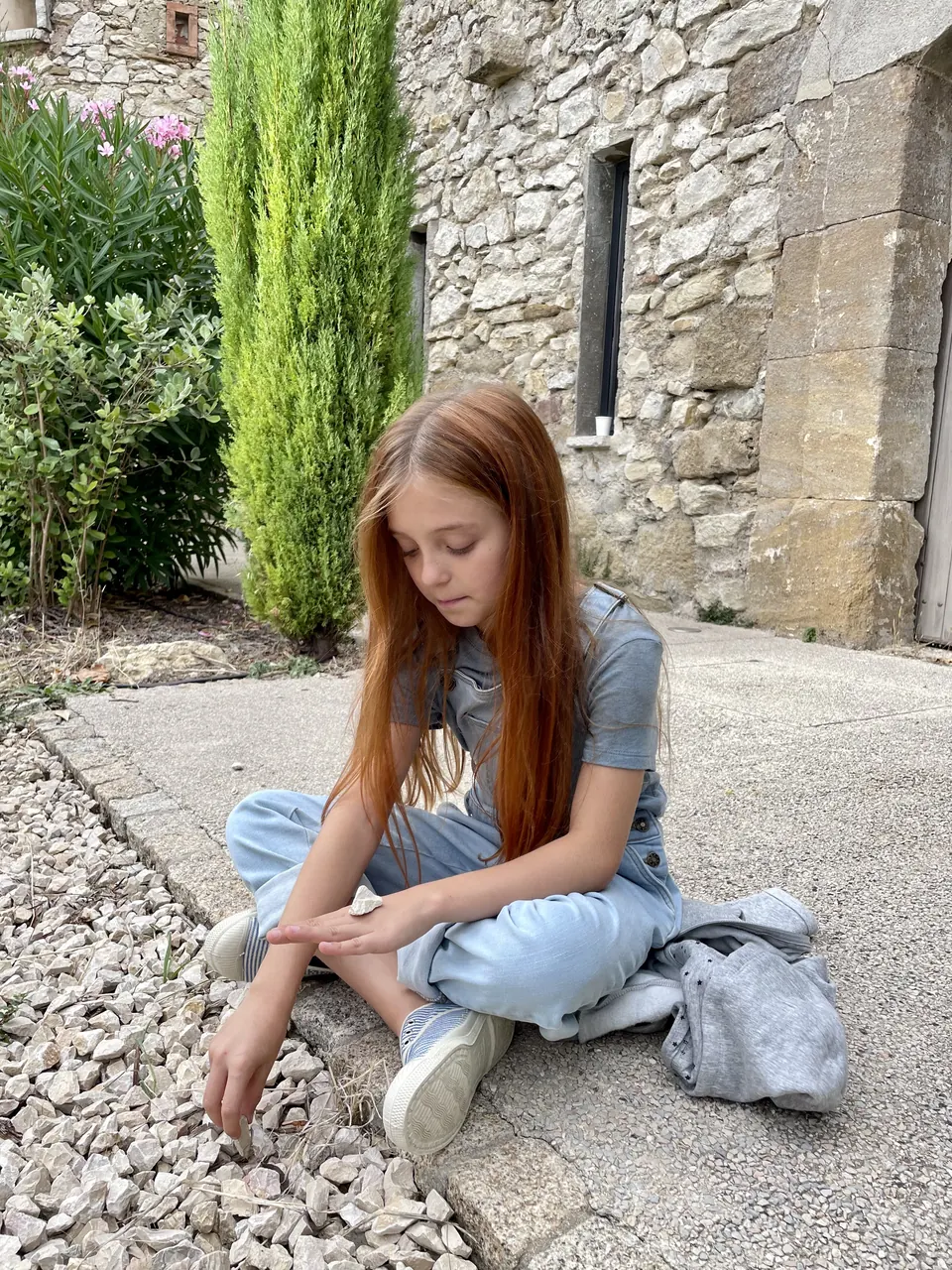 Manon Maindivide casual photo sitting on gravel in denim, by an old stone building