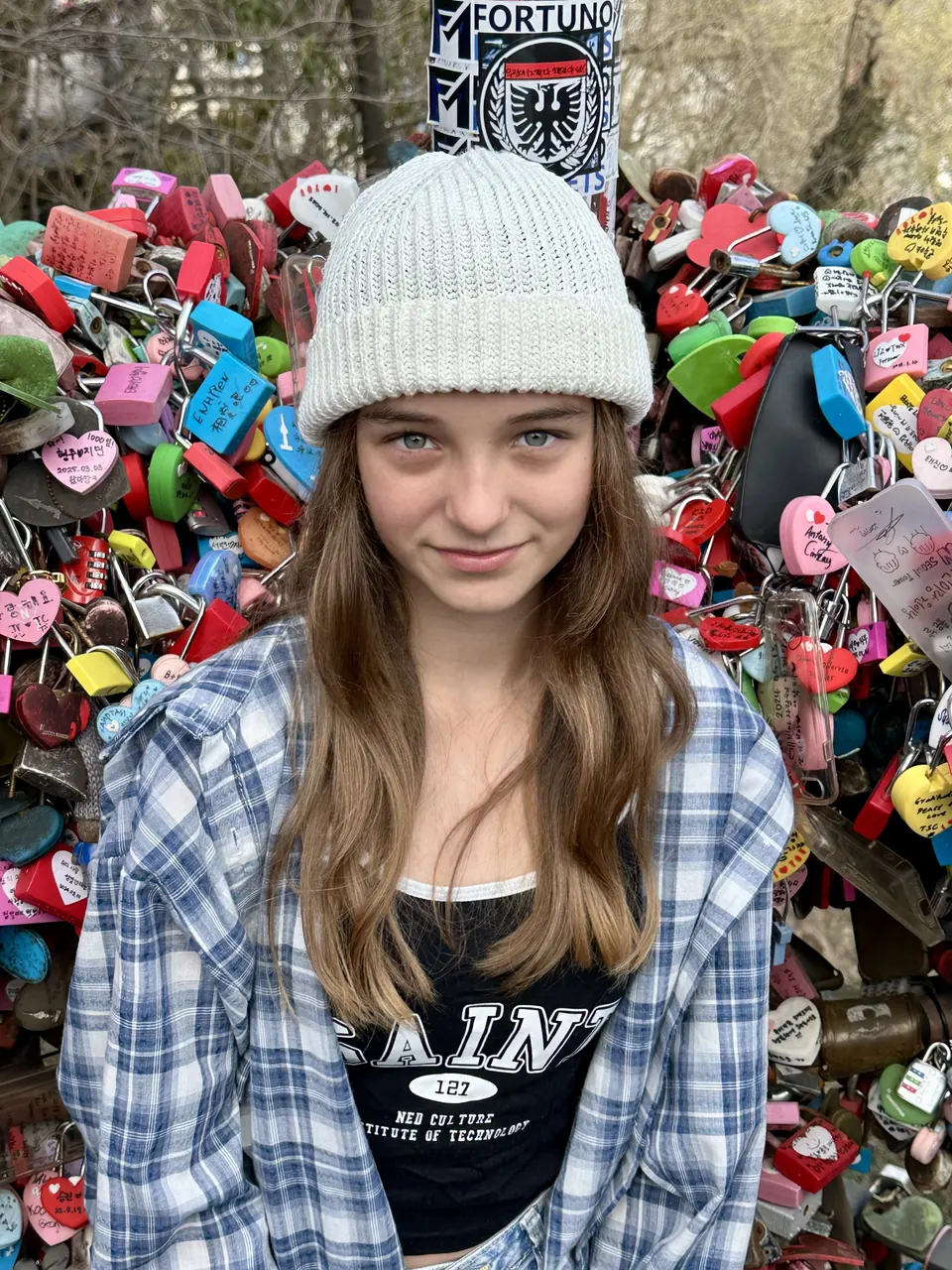 Manon Maindivide casual photo in a grey beanie and plaid shirt in front of a wall of colourful padlocks