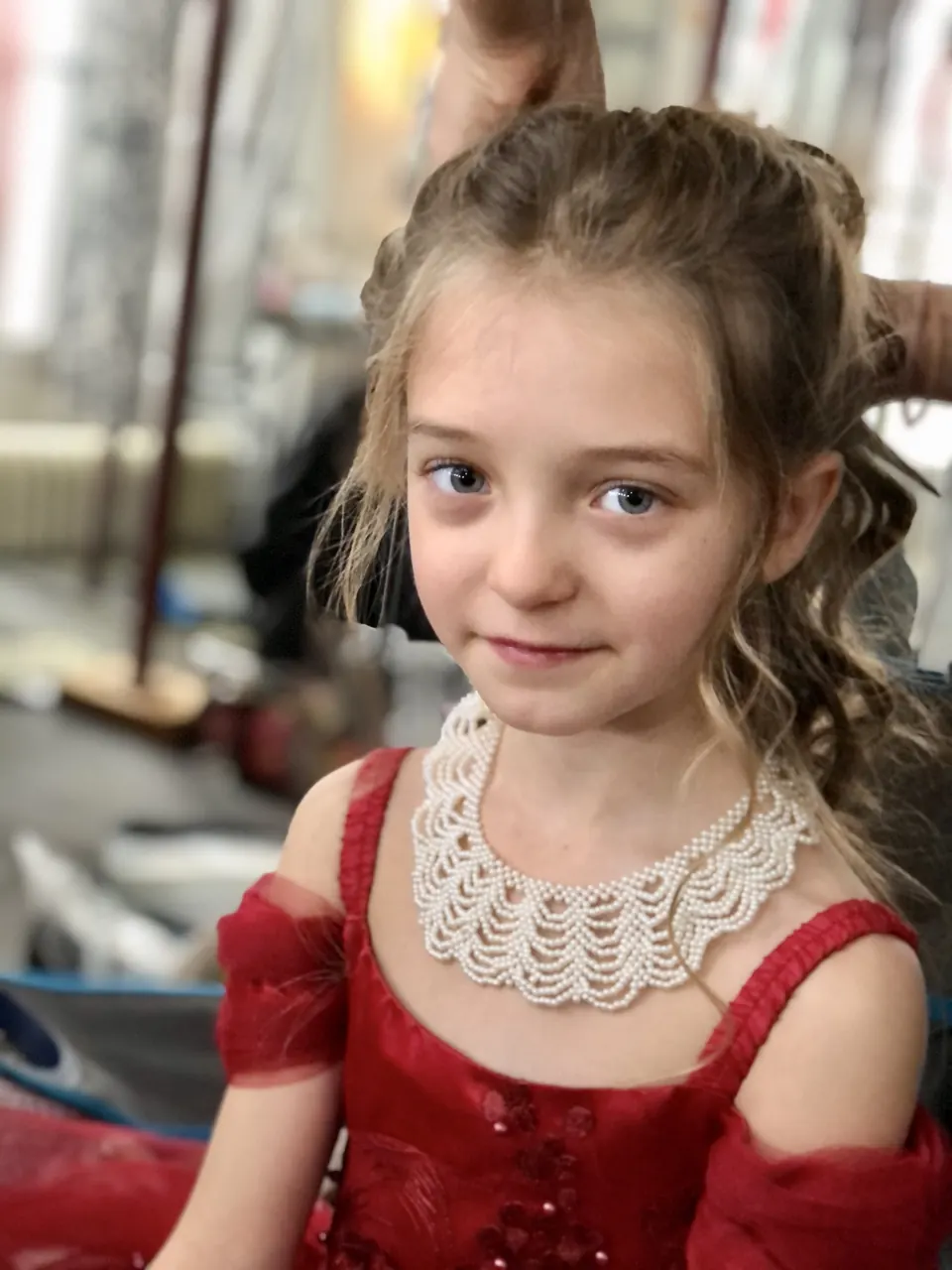 Manon Maindivide behind the scenes in a red costume and pearl collar during hair styling