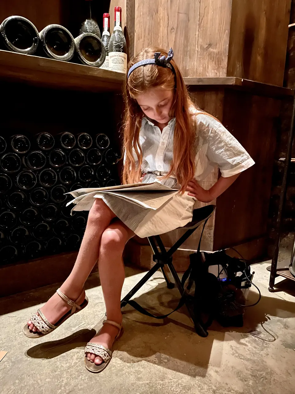 Manon Maindivide behind the scenes, reading a script on a folding chair in a wine cellar set