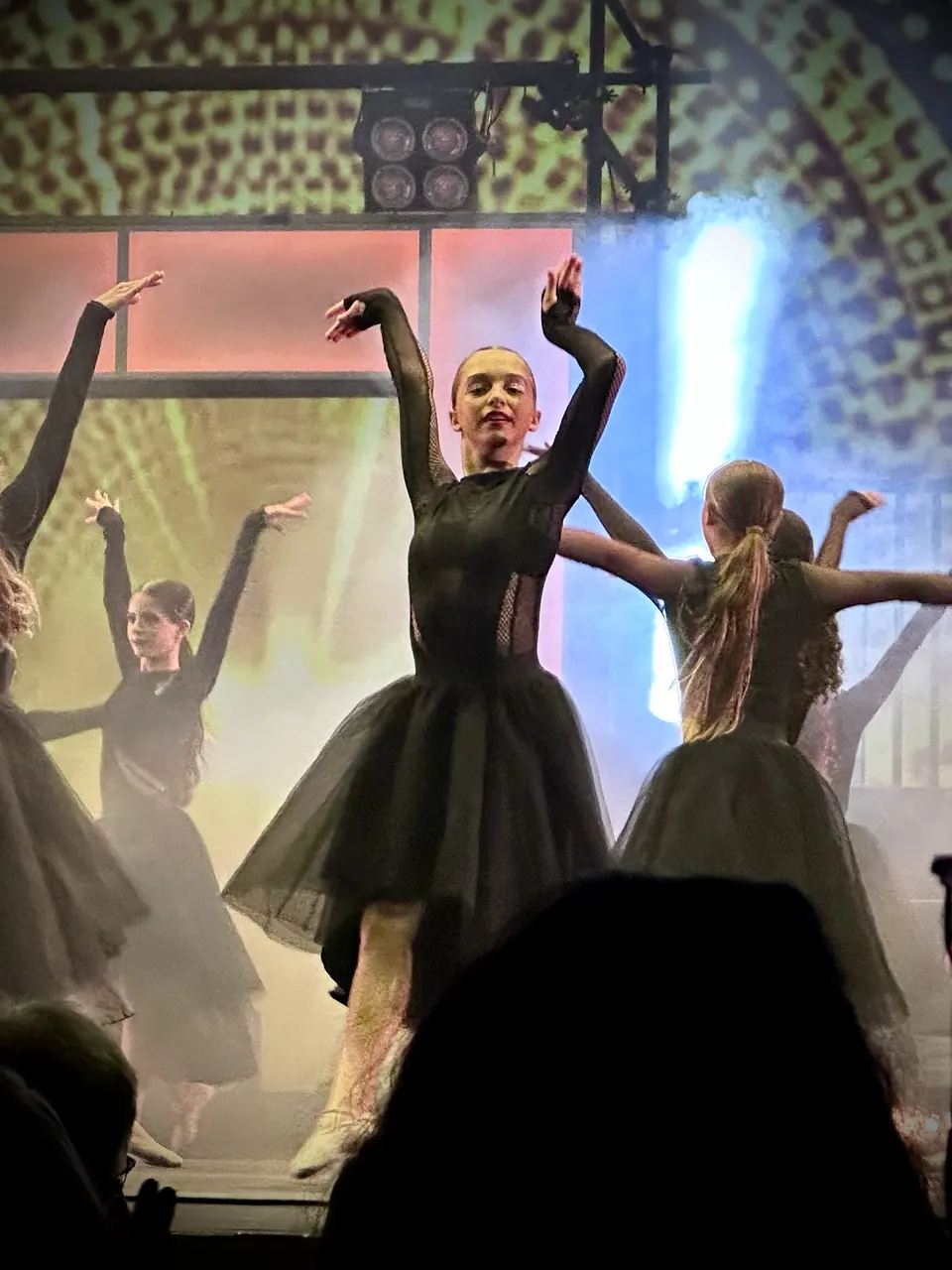Manon Maindivide dance performance in a black tulle dress, arms lifted among other dancers
