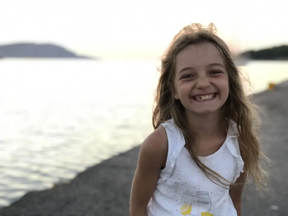 Manon Maindivide casual photo, smiling widely in a white top by the water at sunset