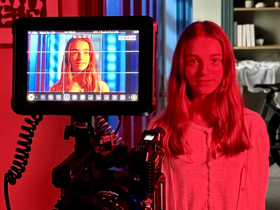 Manon Maindivide on set under red lighting, her image shown on a camera monitor in the foreground
