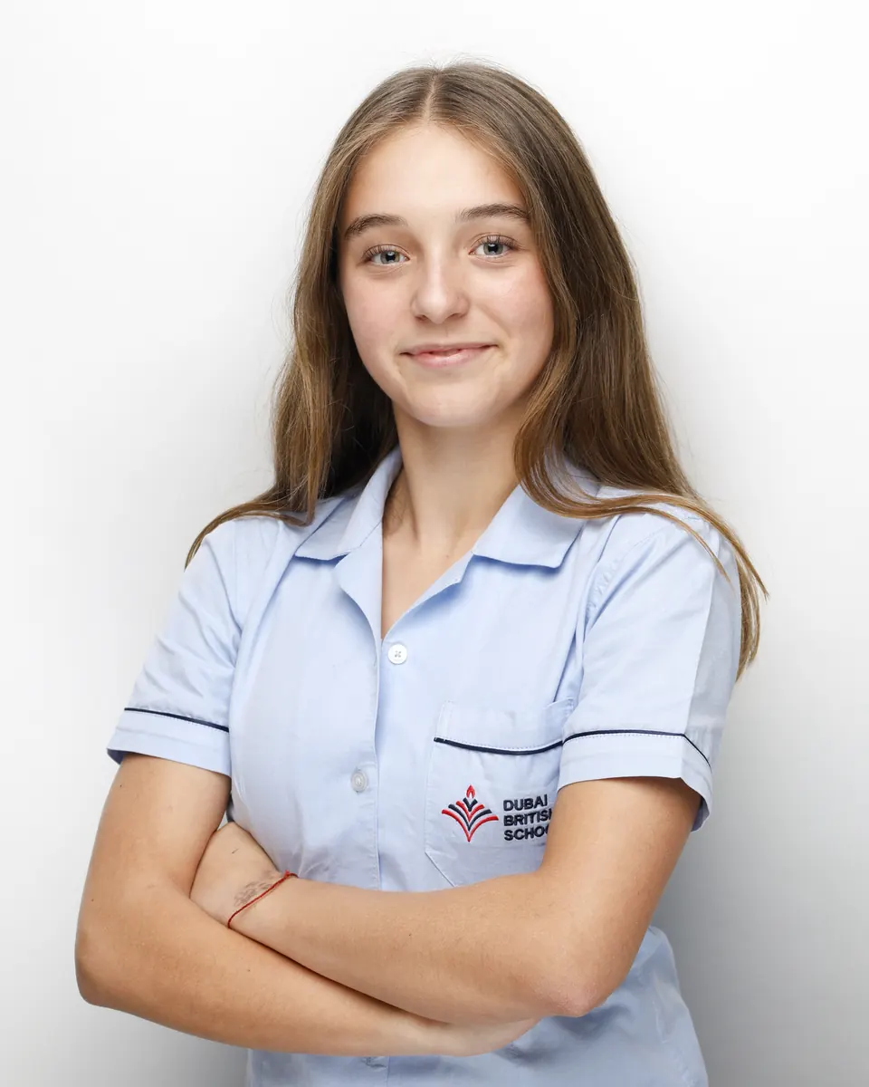 Manon Maindivide headshot in a light blue school shirt with arms crossed, white background