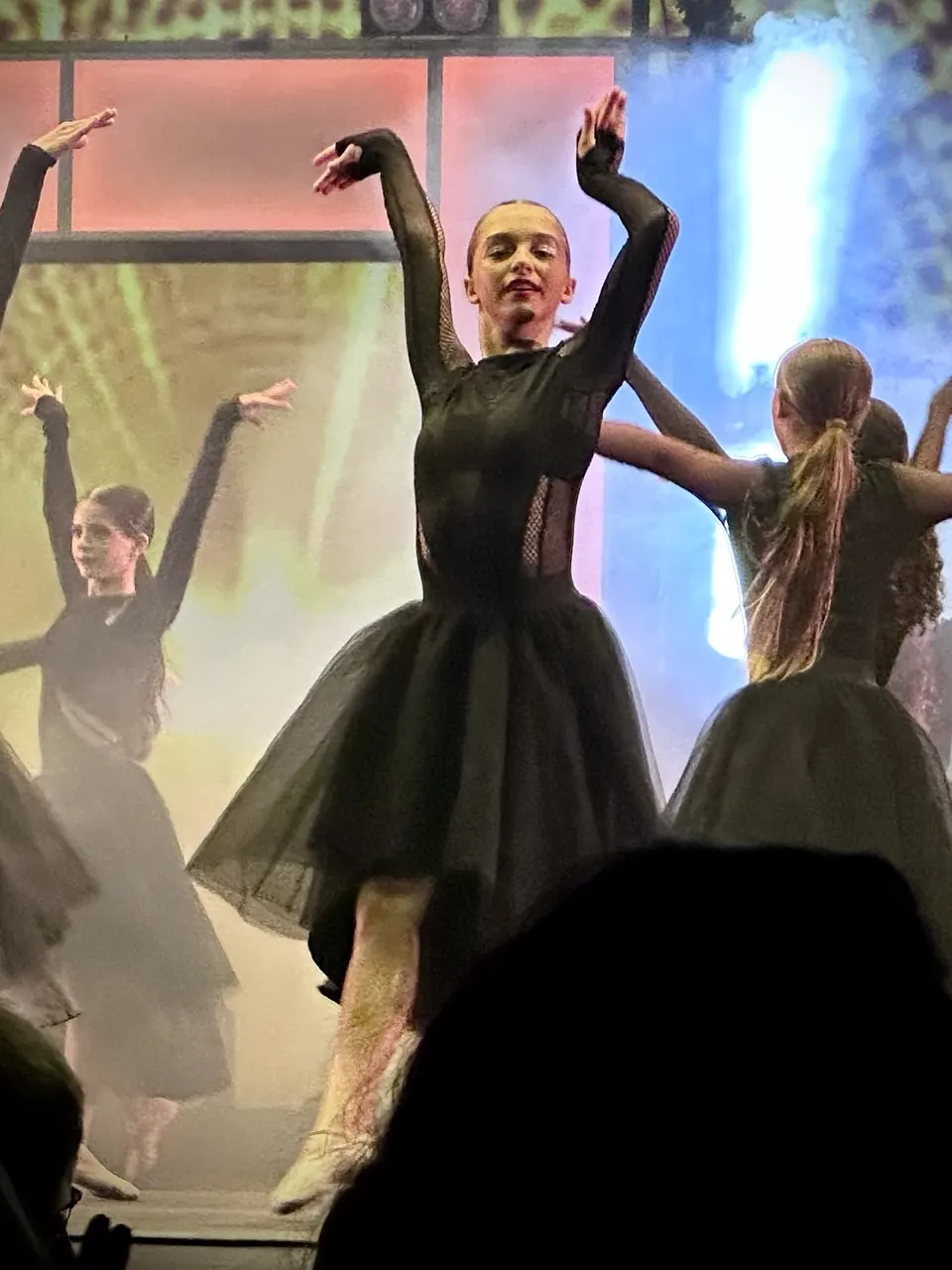 Manon Maindivide dance performance in a black dress, arms raised high with dancers under coloured lights
